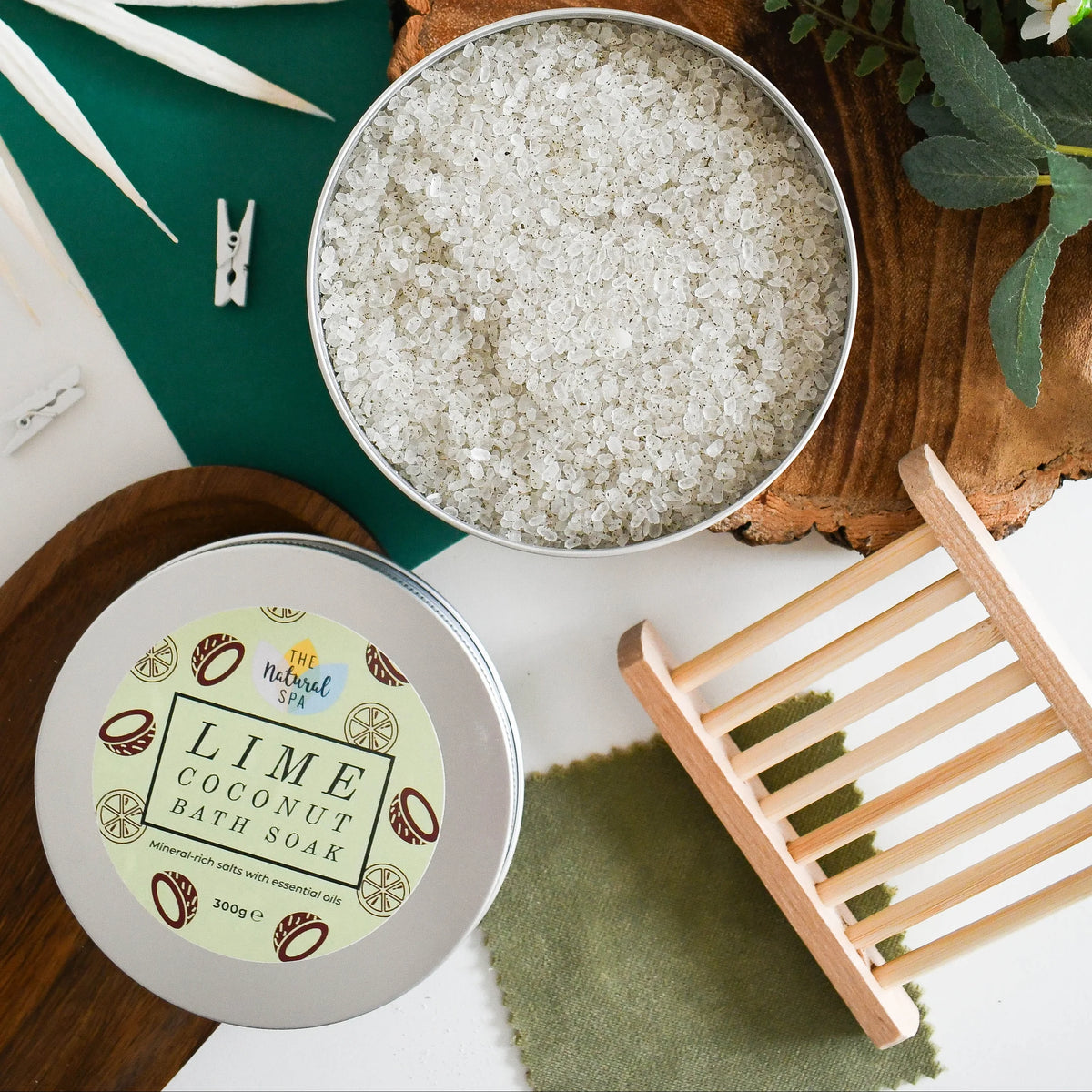 Bath soak container labeled 'Lime Coconut' with a wooden scoop on a green surface.