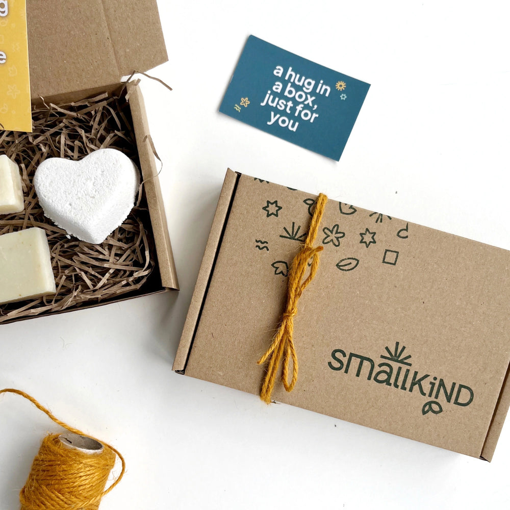 Close up of a Smallkind gift box with the logo and brand patter hand stamped in green ink. The box is tied with mustard twine and there is a small green card which says 'a hug in a box, just for you'