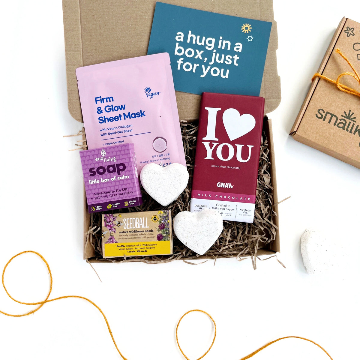 Love You Letterbox Gift: Eco-friendly pampering box with face mask, bath bombs, ethical chocolate, and wildflower seeds for bees. The products have a purple theme and are inside a hand stamped kraft gift box. 
