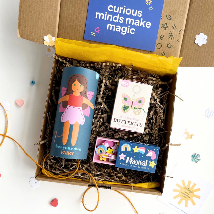 children's gift box with fairy-themed items including a sewing kit and jewellery making kit with 'curious minds make magic' text on a blue gift card.