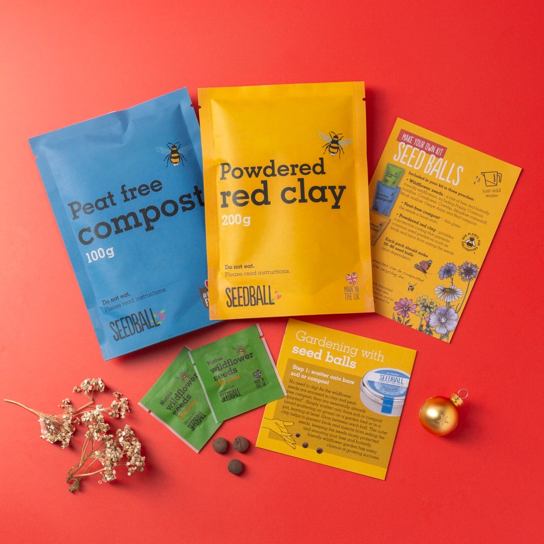 contents of make your own seedball kit including compost, clay, wildflower seeds and instructions laid flat on a red background