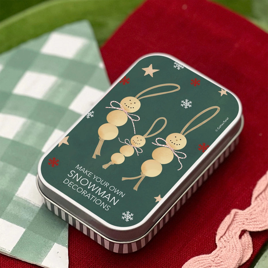 Decorative tin with snowman design on a checkered surface. Cotton Twist Make Your Own Snowman Decorations craft kit. Age 3+