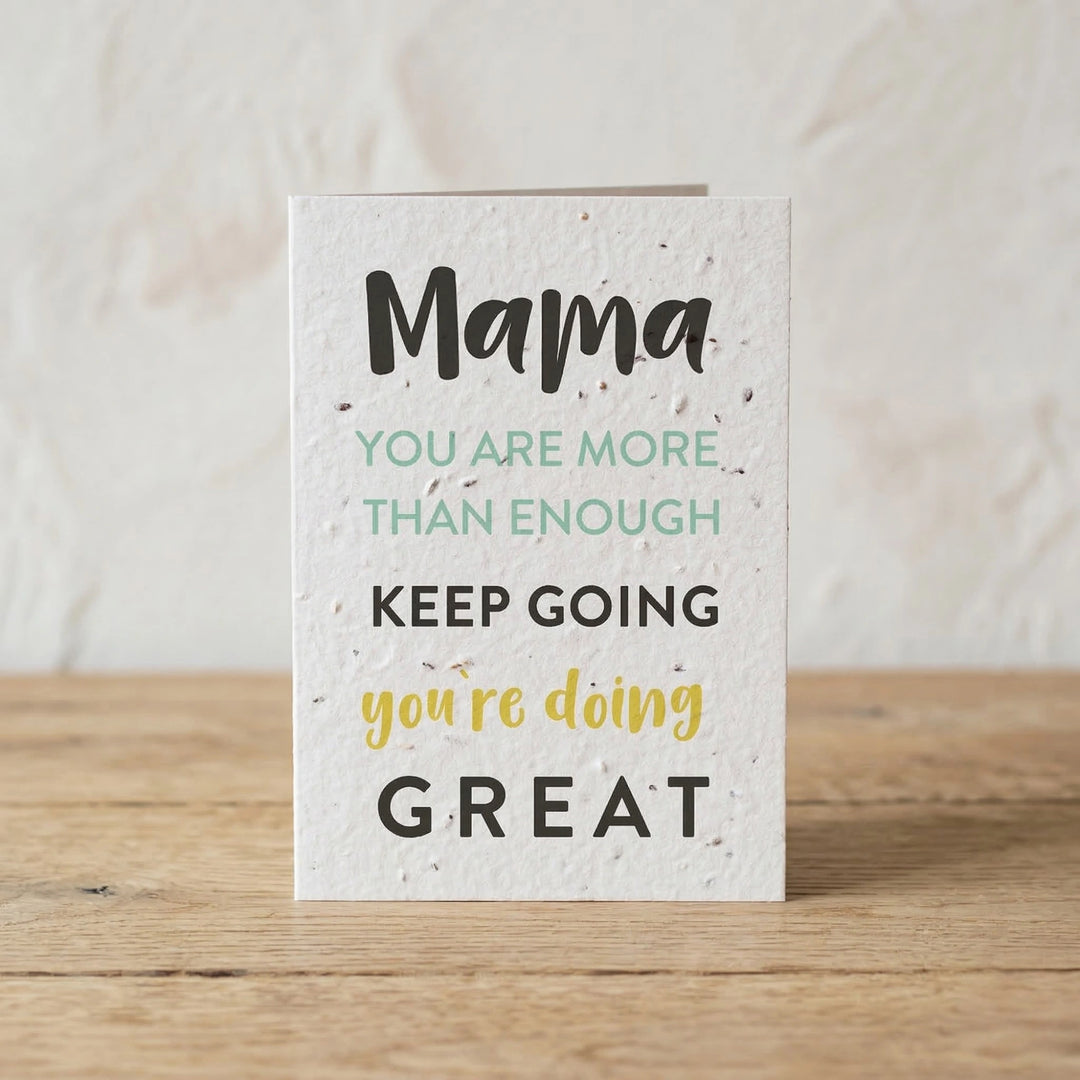Motivational card with text 'Mama you are more than enough, keep going, you're doing great' on a wooden surface.