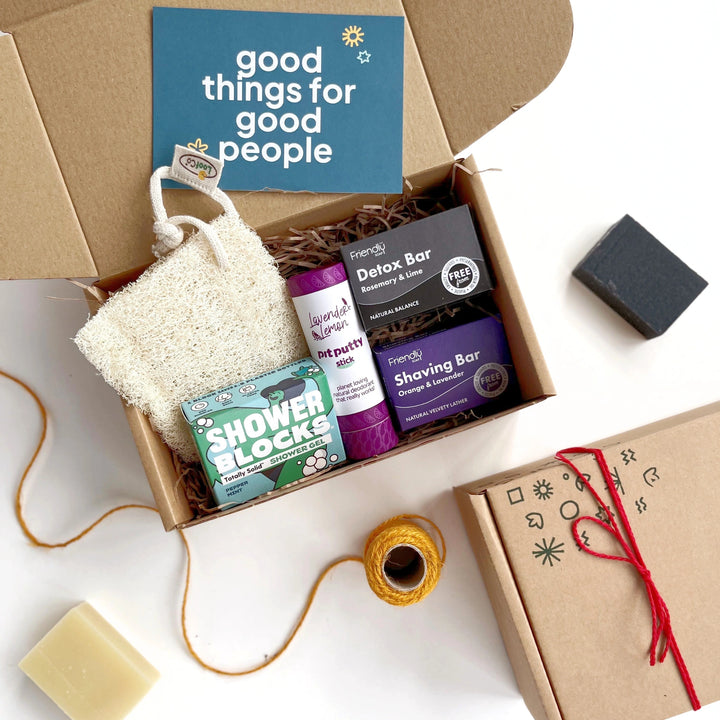 mens deluxe eco grooming box with a natural deodorant, detox soap bar, shaving soap bar, loofah and peppermint shower gel bar. The products have a blue and purple theme and are inside a kraft gift box with shredded paper. 