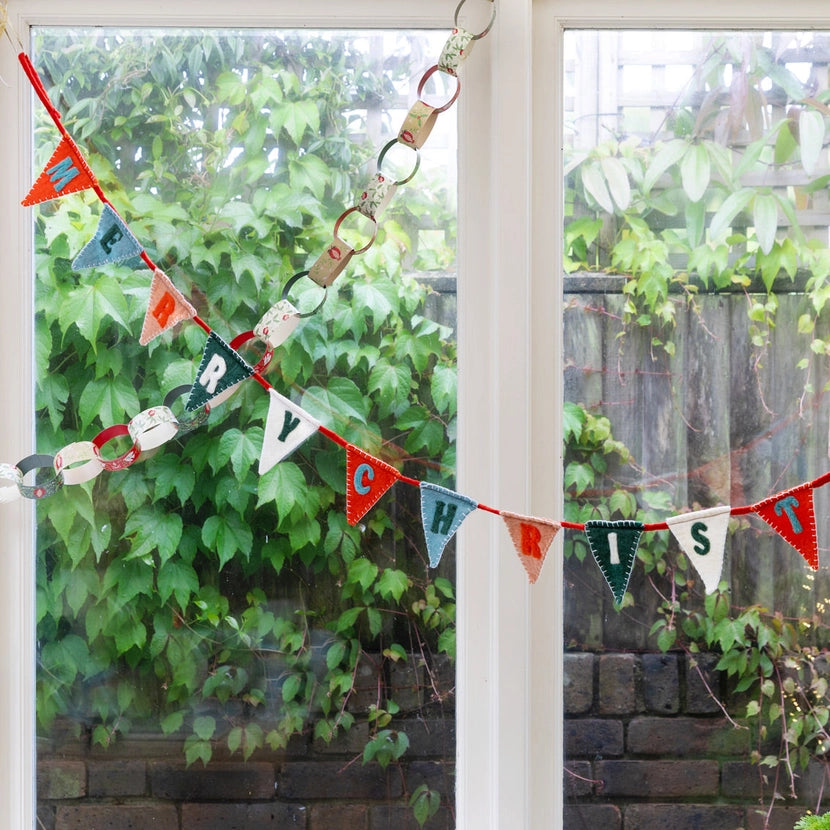 Decorative merry Christmas bunting with colourful letters hanging on a glass door with green foliage in the background