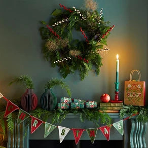 Decorative Christmas mantel with wreath, candles, and festive decor against a dark wall.