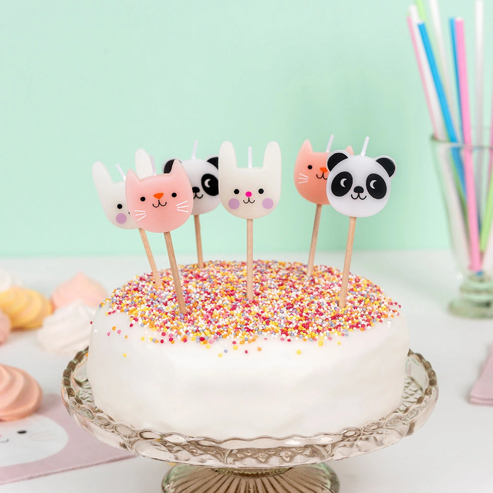 Cake with animal-themed candles - panda, cat and bunny -  on a white cake against a light green background