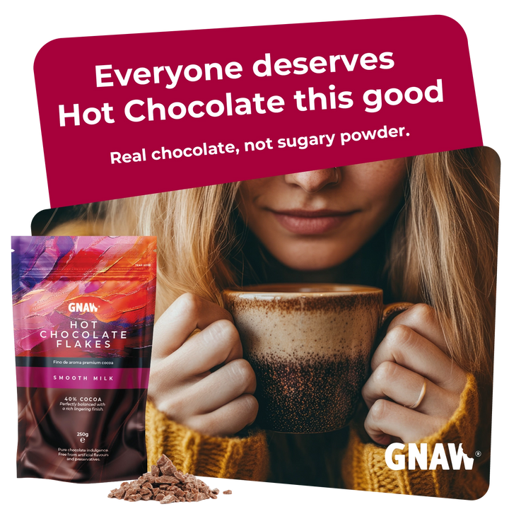 A promotional product image for GNAW Hot Chocolate Flakes. On the left is a stand-up pouch of Smooth Milk flavor hot chocolate flakes, with a small pile of the flakes in front.