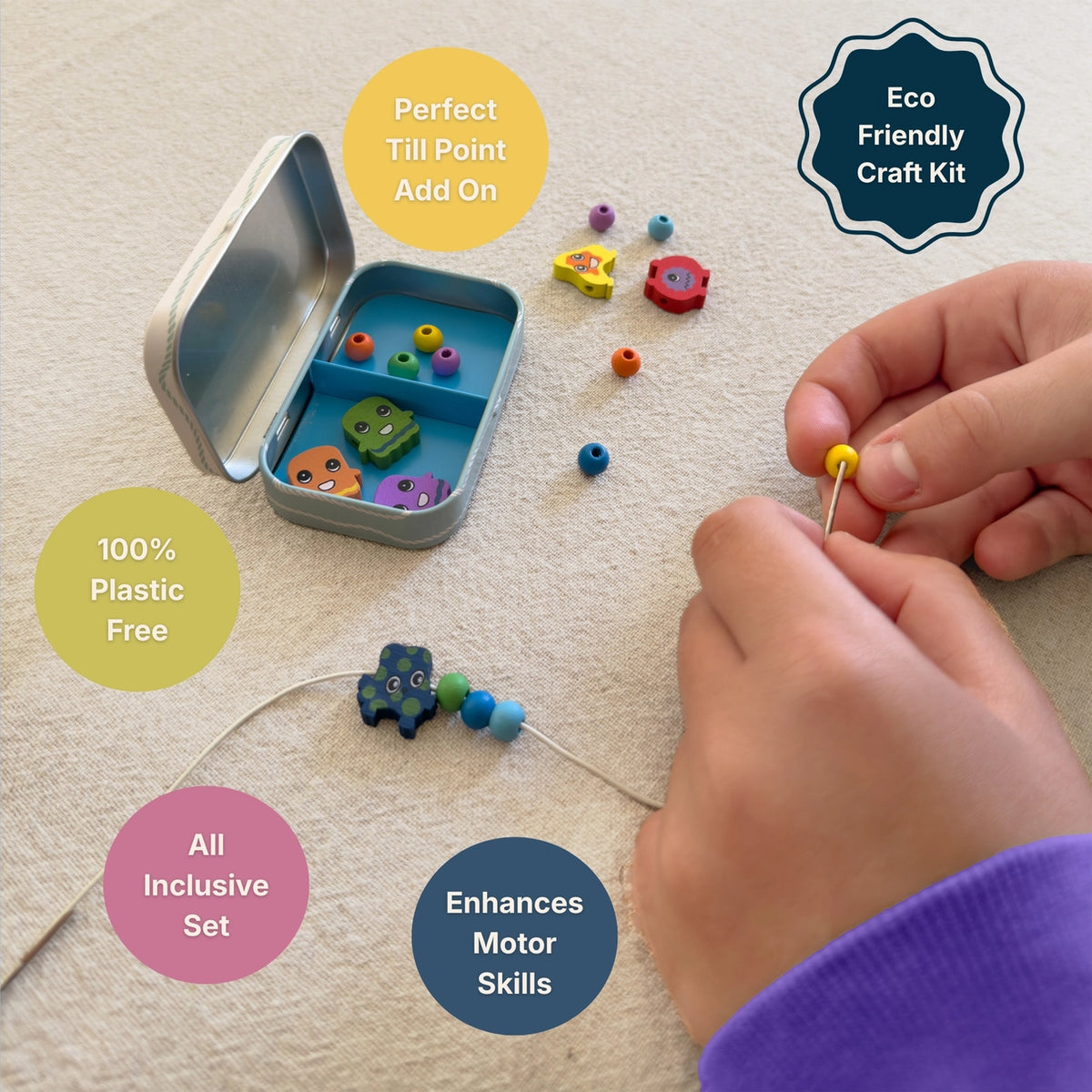 A close-up of a child's hands threading colorful wooden beads onto a string, with a small metal tin of beads and loose craft pieces nearby on a beige fabric surface. Text callouts describe the eco-friendly craft kit, plastic-free materials, all-inclusive set, and motor skills benefit.
