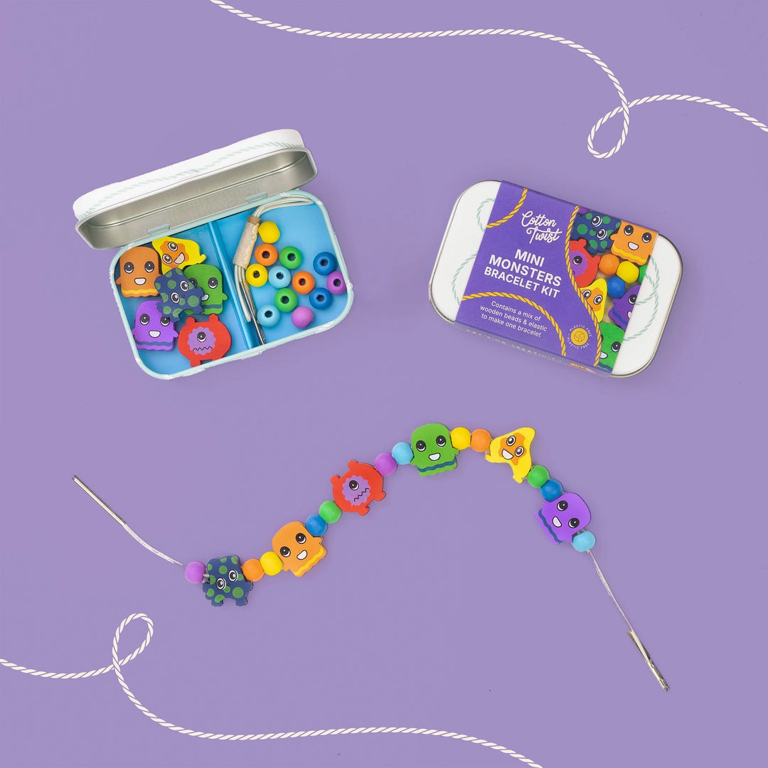 Mini Monsters Bracelet Kit by The Magic Shop, showing an open tin filled with colourful beads, a packaged product box, and a completed beaded bracelet laid out on a purple background.
