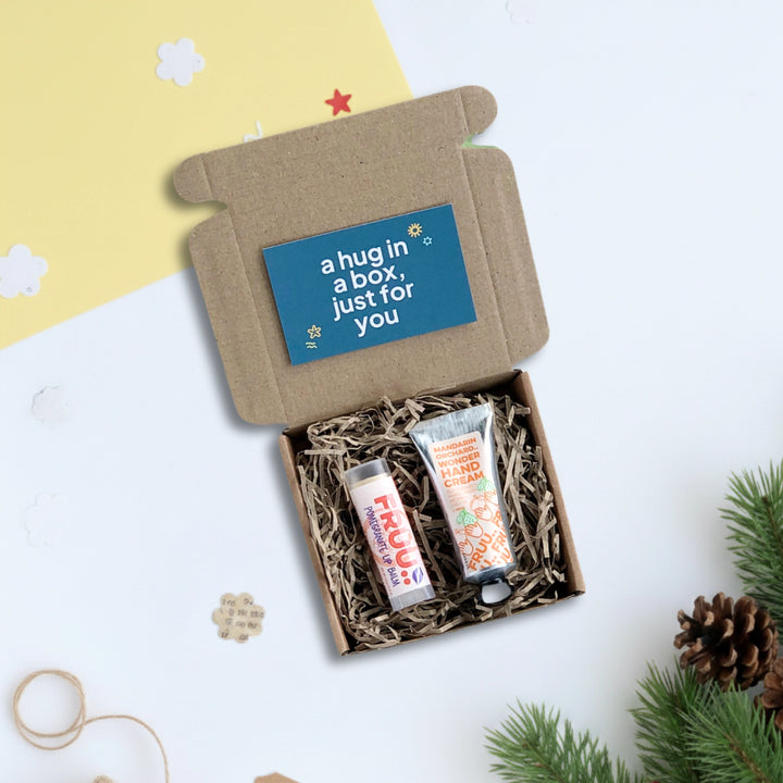 mini gift box with pomegranate lip balm and mandarin orchard hand cream on a light background with pinecones