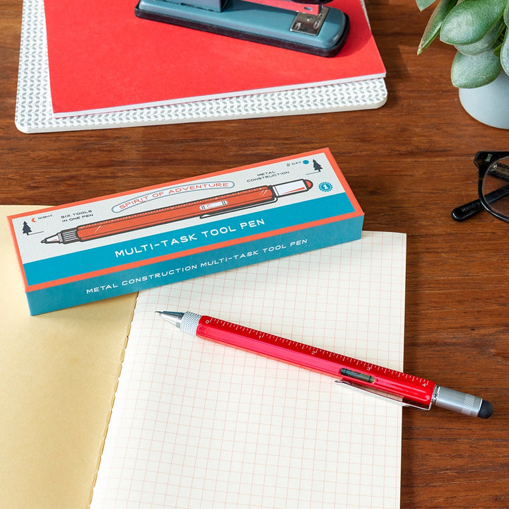 Red multi-task tool pen with packaging on a desk with stationery items.