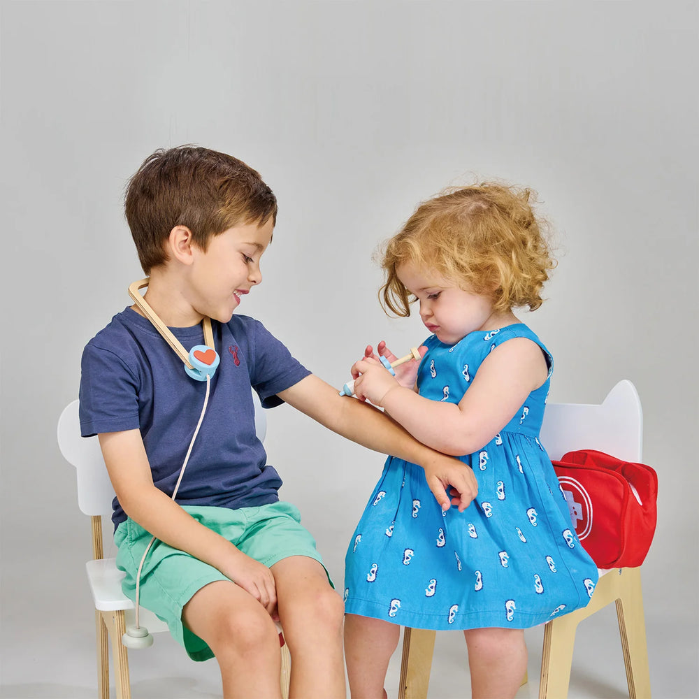 Two children playing doctor with medical toys on a plain background