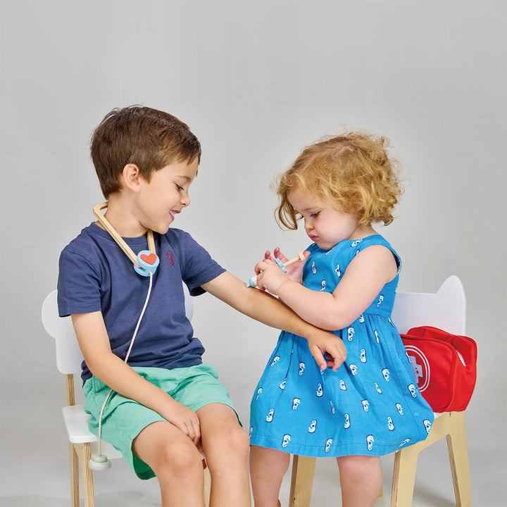 Two children playing doctor with medical toys on a plain background