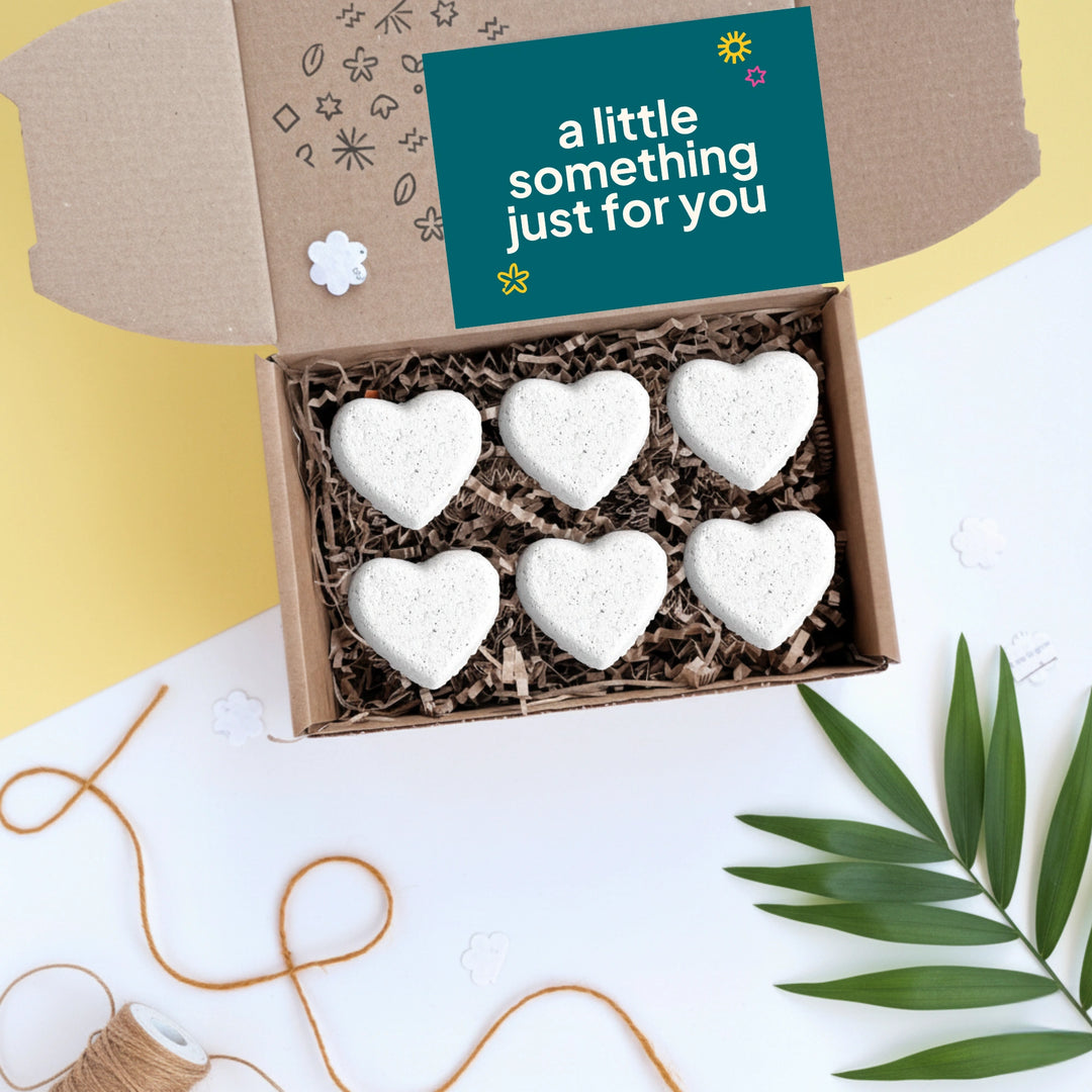 Box of heart-shaped bath bombs with a card reading 'a little something just for you' on a decorative background.