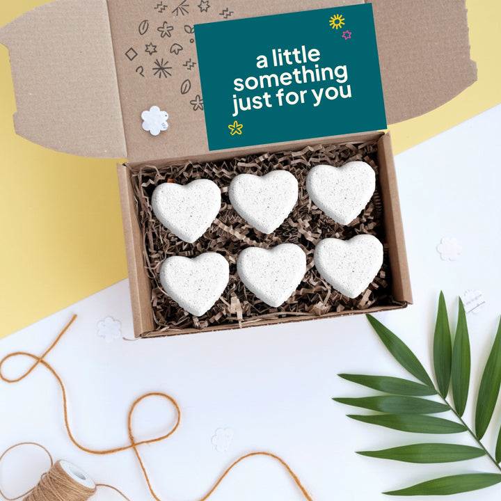 Box of heart-shaped bath bombs with a card reading 'a little something just for you' on a decorative background.