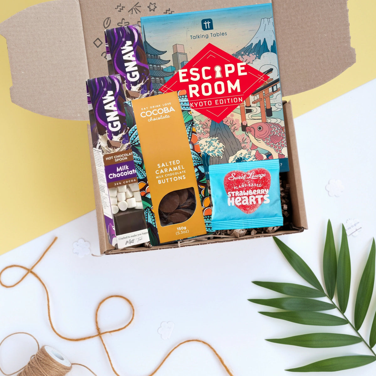 Box of chocolate bars and sweets with 'Escape Room' game on a white surface with decorative elements.