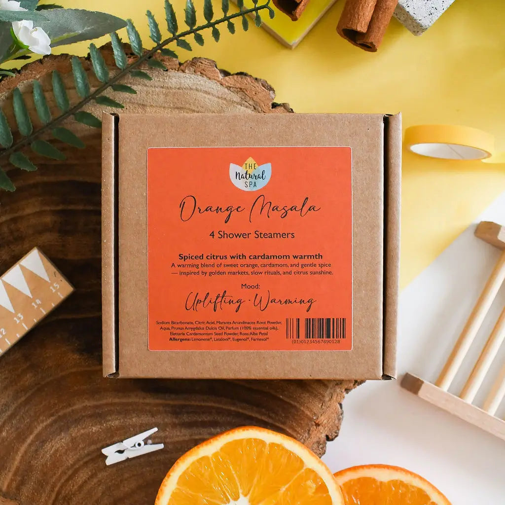 Box of Orange Masala shower steamers with an orange slice and cinnamon sticks on a wooden surface.