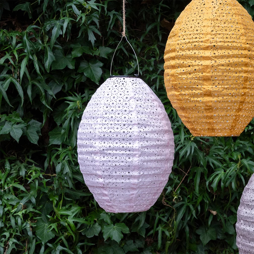 Two hanging lanterns, one soft pink and one yellow, against a green leafy background.