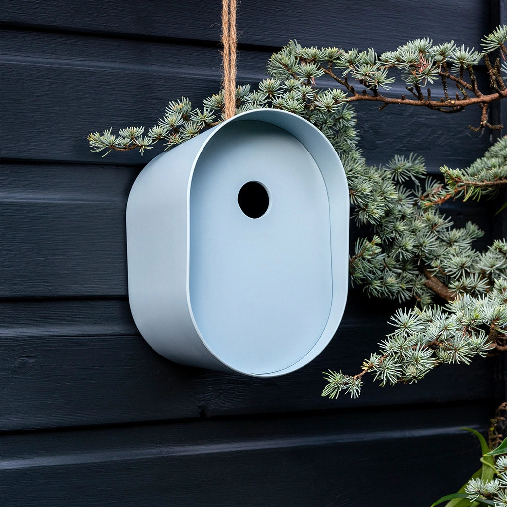  Rex London Oval Bamboo Bird House in pastel blue hanging on a dark grey fence. 