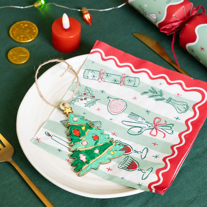 Christmas-themed card with a tree ornament on a plate, surrounded by festive items.