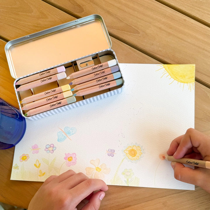 childs hands drawing flowers with coloured pencils on a wooden table