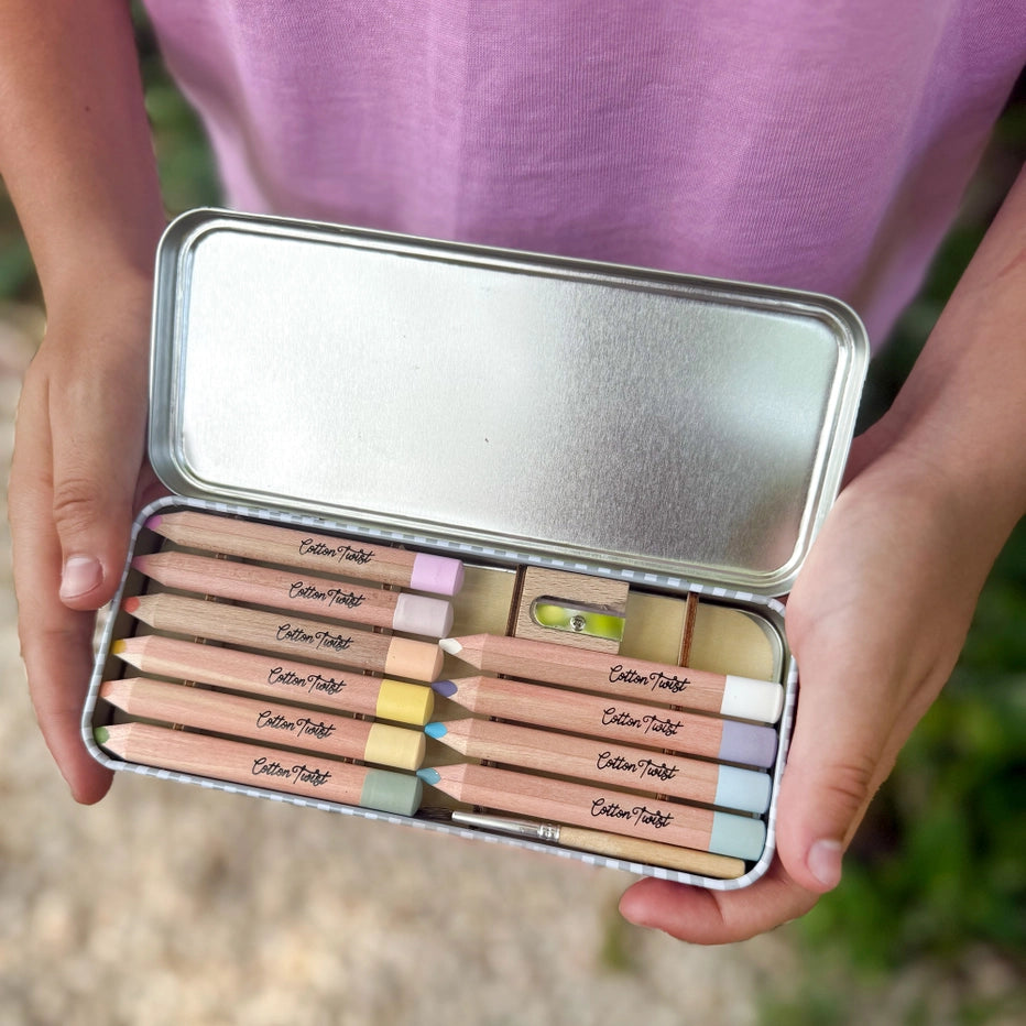 Childs hands holding a set of coloured pencils in a metal case with a blurred background