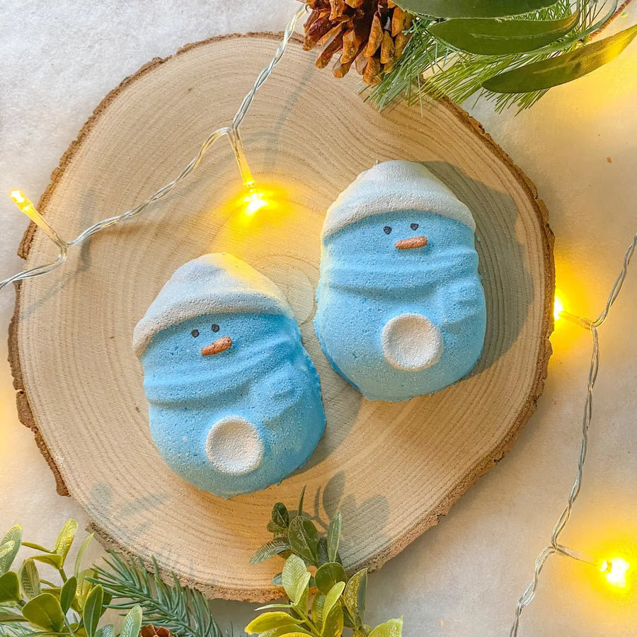 two blue penguin bath bombs on a neutral wooden background with festive holly branches