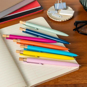 Colourful pens on a notebook with office supplies in the background