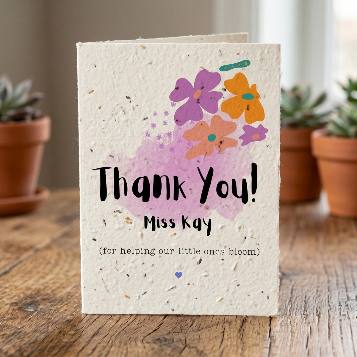 Greeting card with flowers and 'Thank You! Miss Kay' text on a wooden surface with plants in the background