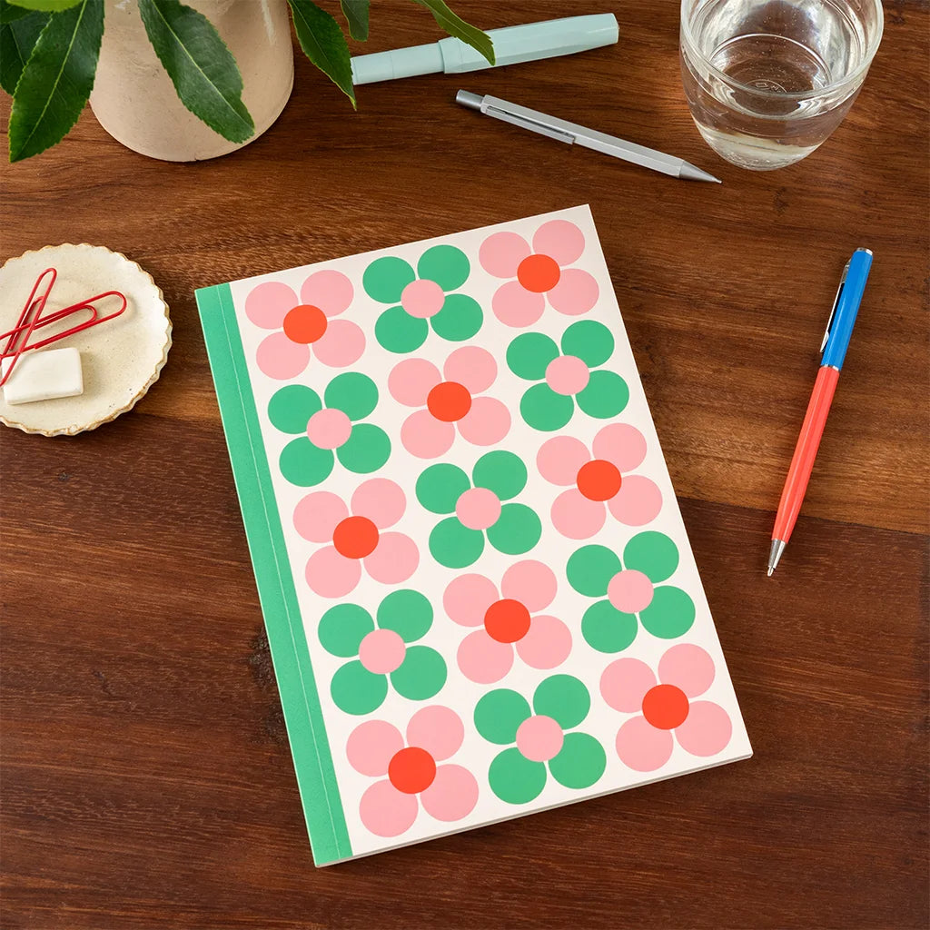Notebook with floral design on a wooden surface with stationery items.