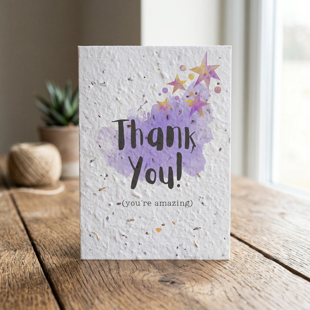 Greeting card with 'Thank You! (you're amazing)' text and purple watercolor design on a wooden surface.