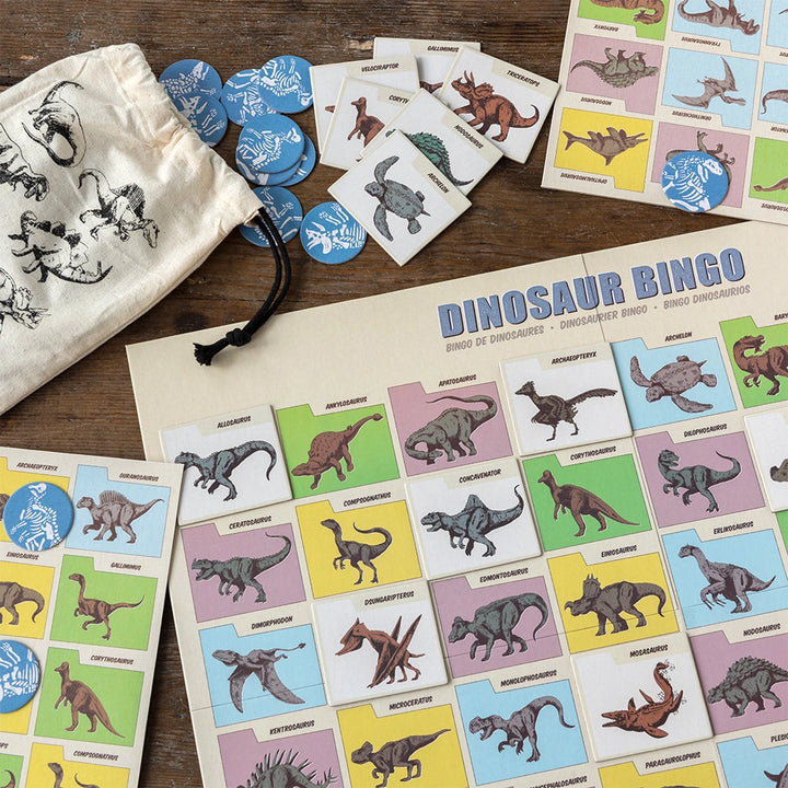 Dinosaur bingo game set with cards, markers, and a bag on a wooden surface