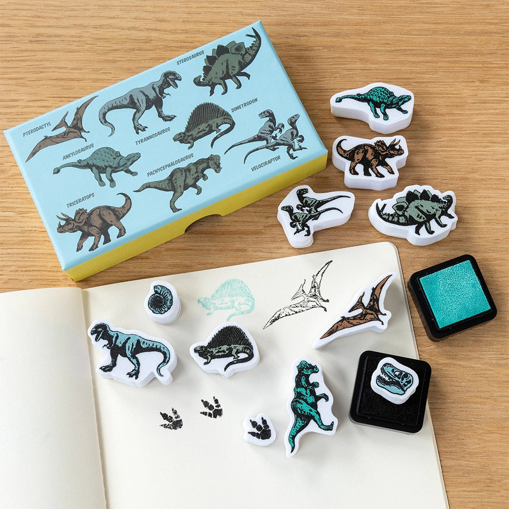 Dinosaur-themed stamp set with stamps, ink pad, and illustrated dinosaur storage box on a wooden surface