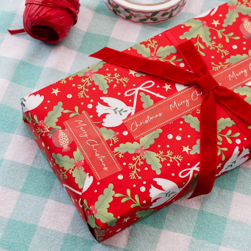 Red Christmas-themed gift box with a bow and red merry Christmas paper tape on a checkered tablecloth