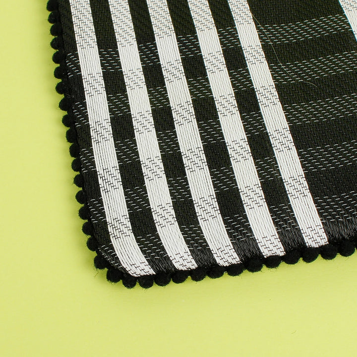 close up of black and white checked pouch with a black zip and pom pom trim around the edges. Made from recycled cement sacks. 