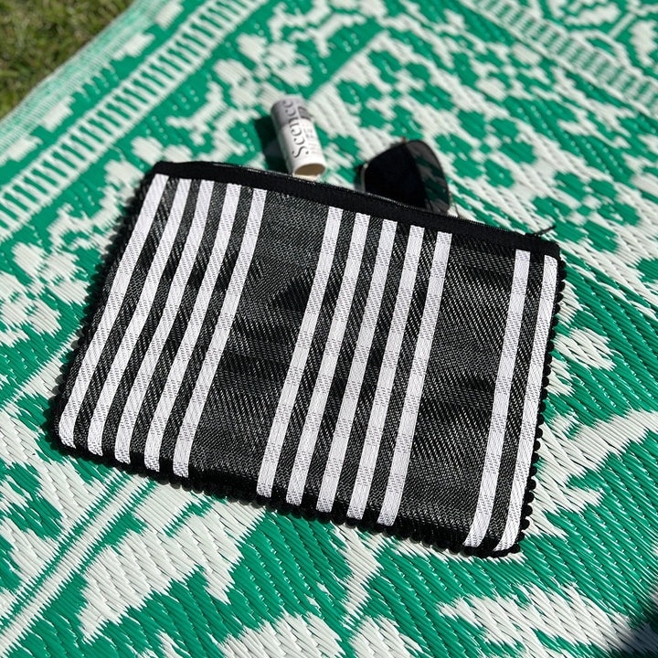 black and white checked pouch with a black zip and pom pom trim around the edges. the pouch is open with a lip balm and sunglasses inside