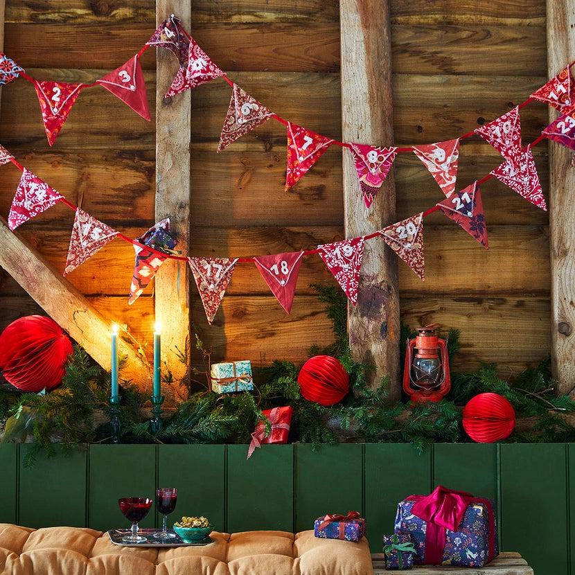 festive decorations including red and white reusable Christmas advent calendar bunting, lanterns, and presents against a wooden wall.