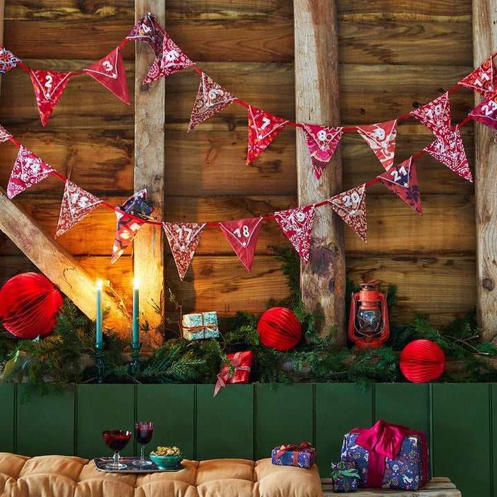 festive decorations including red and white reusable Christmas advent calendar bunting, lanterns, and presents against a wooden wall.