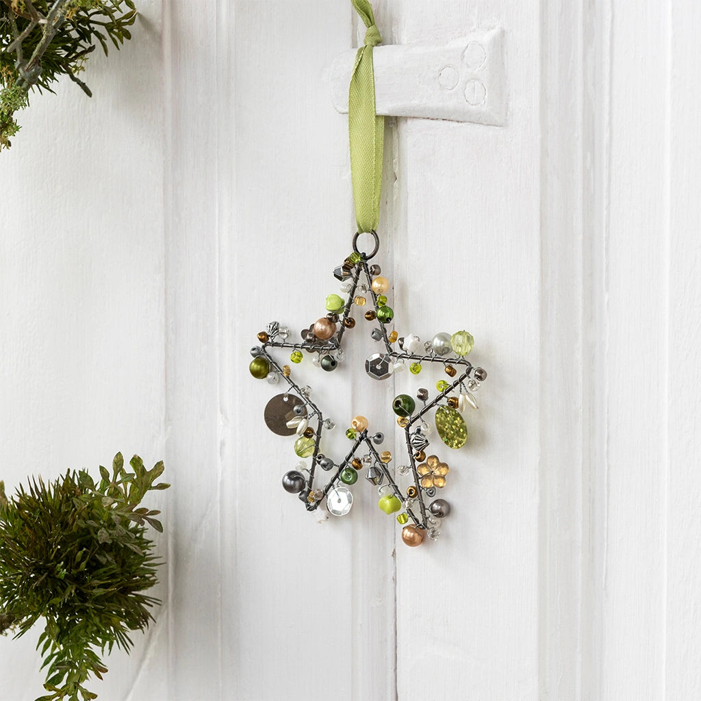 handmade silver star shaped hanging decoration embellished with green beads and hung with a green ribbon. The decoration is hung on a door handle.