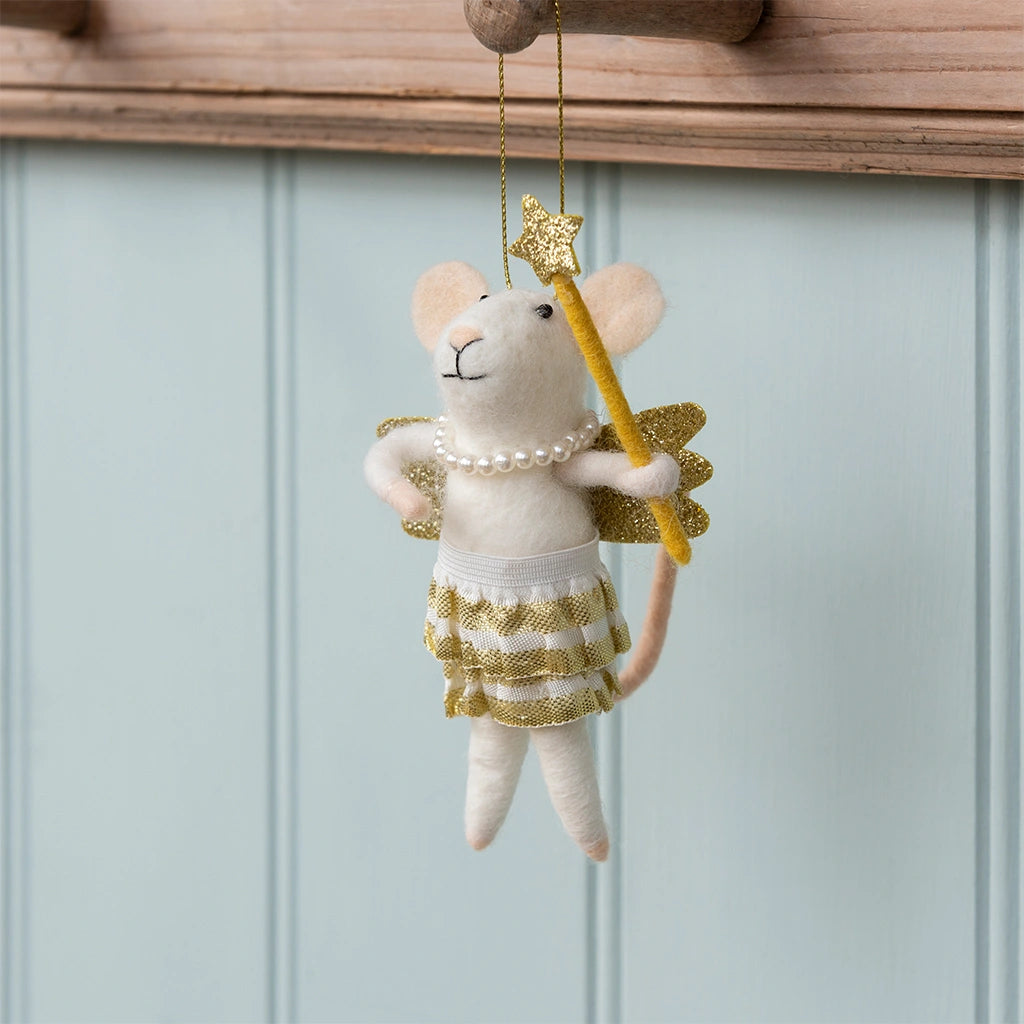 Decorative mouse ornament with gold skirt and wand hanging against a light blue wall.