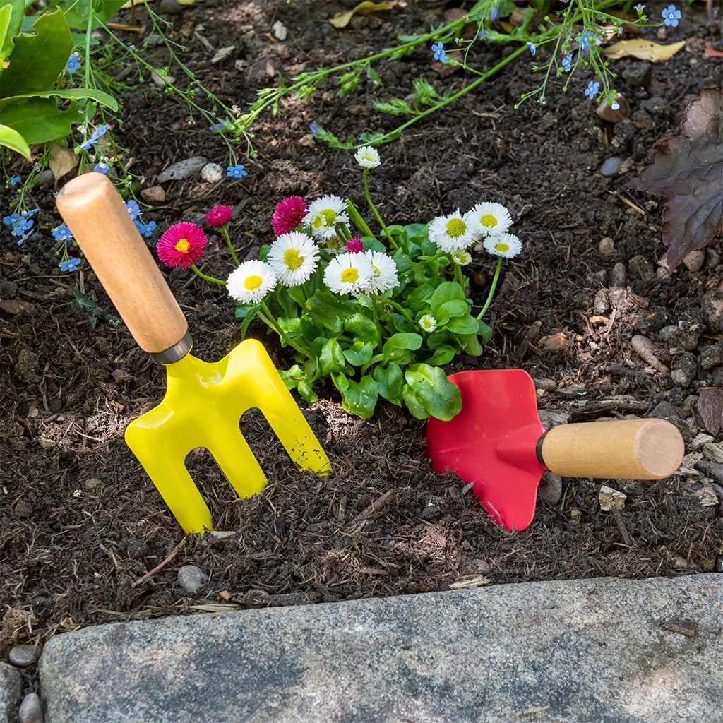 Children's red and yellow Ladybird Gardening Tools with wooden handles  in a raised bed outdoors