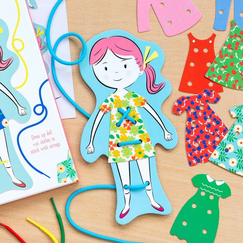 close up of the dress up dolly learn to stitch activity kit for kids age 3 and over. The kit comes with a cardboard doll, pieces of retro clothing and cords to stitch on the outfits. 