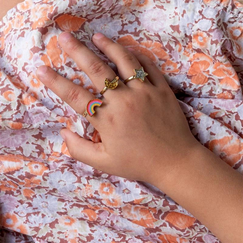 Little girls hand wearing three children's glitter rings in rainbow, moon and star shapes. 