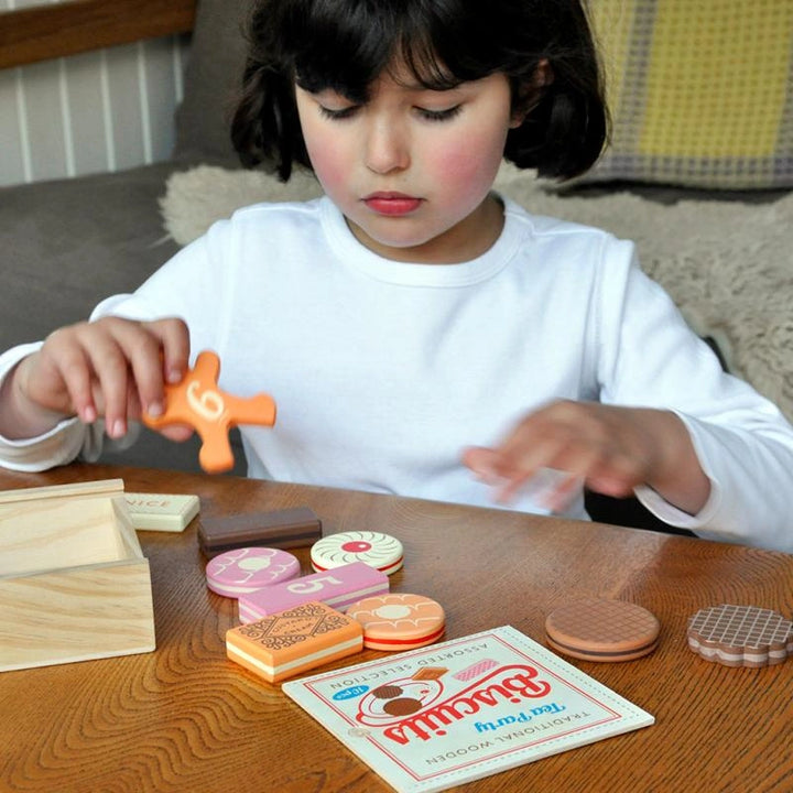 girl with dark hair and white skin playing with rex london wooden traditional tea party biscuits