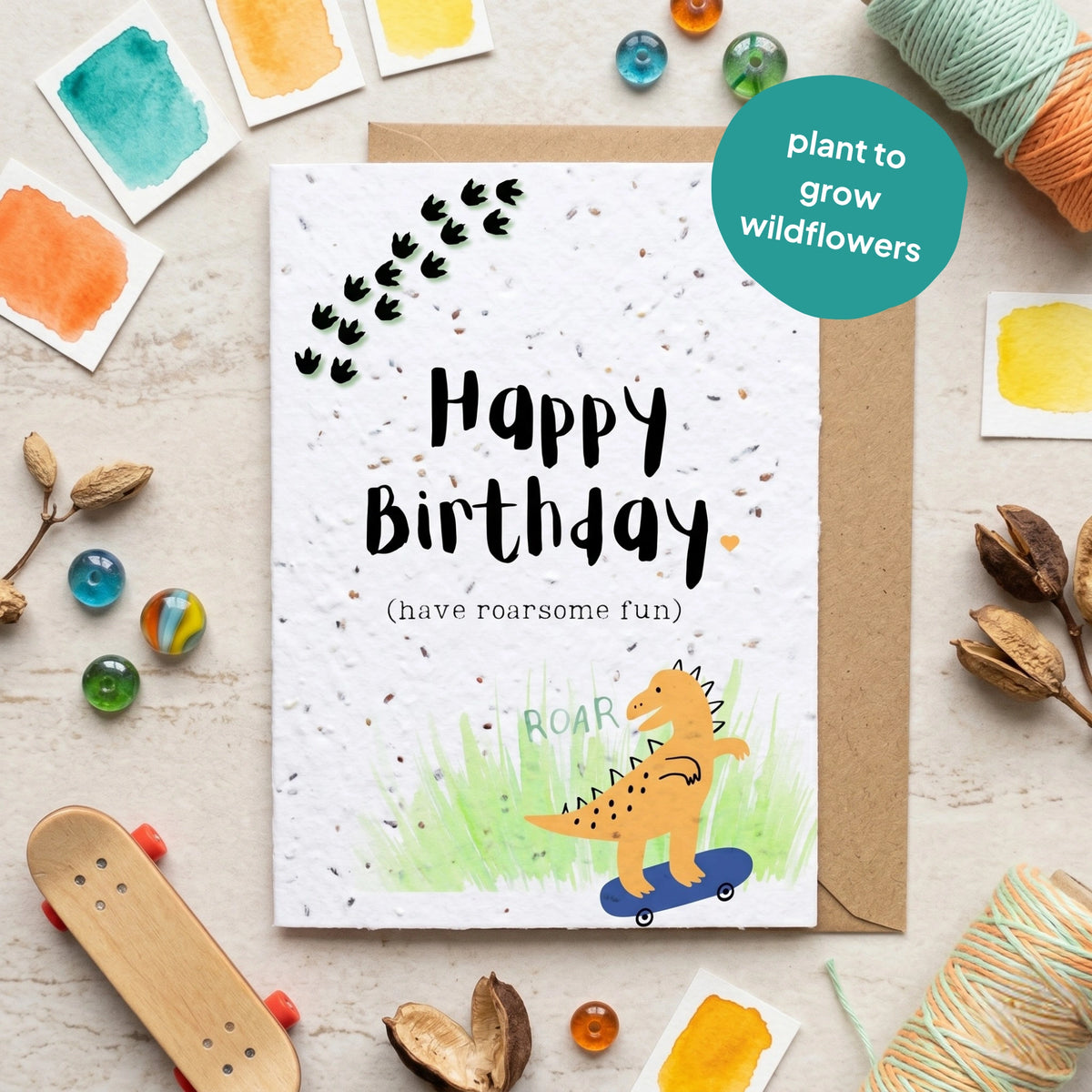 Birthday card with dinosaur illustration and plantable seeds, surrounded by decorative items on a light surface.