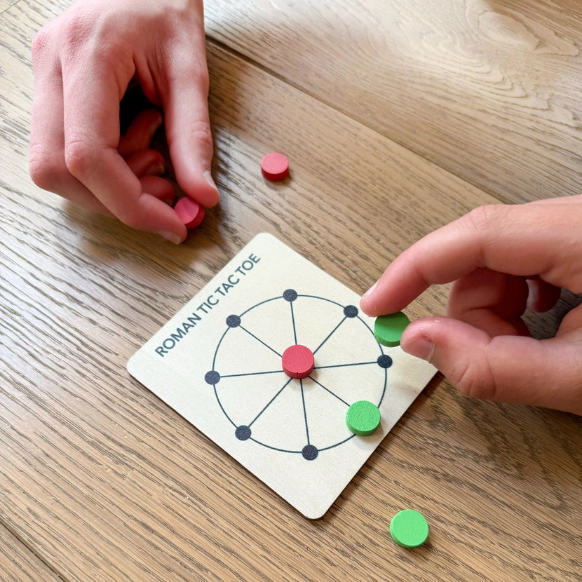 Two hands playing a roman tic tac toe game with colourful circular tokens on a wooden table