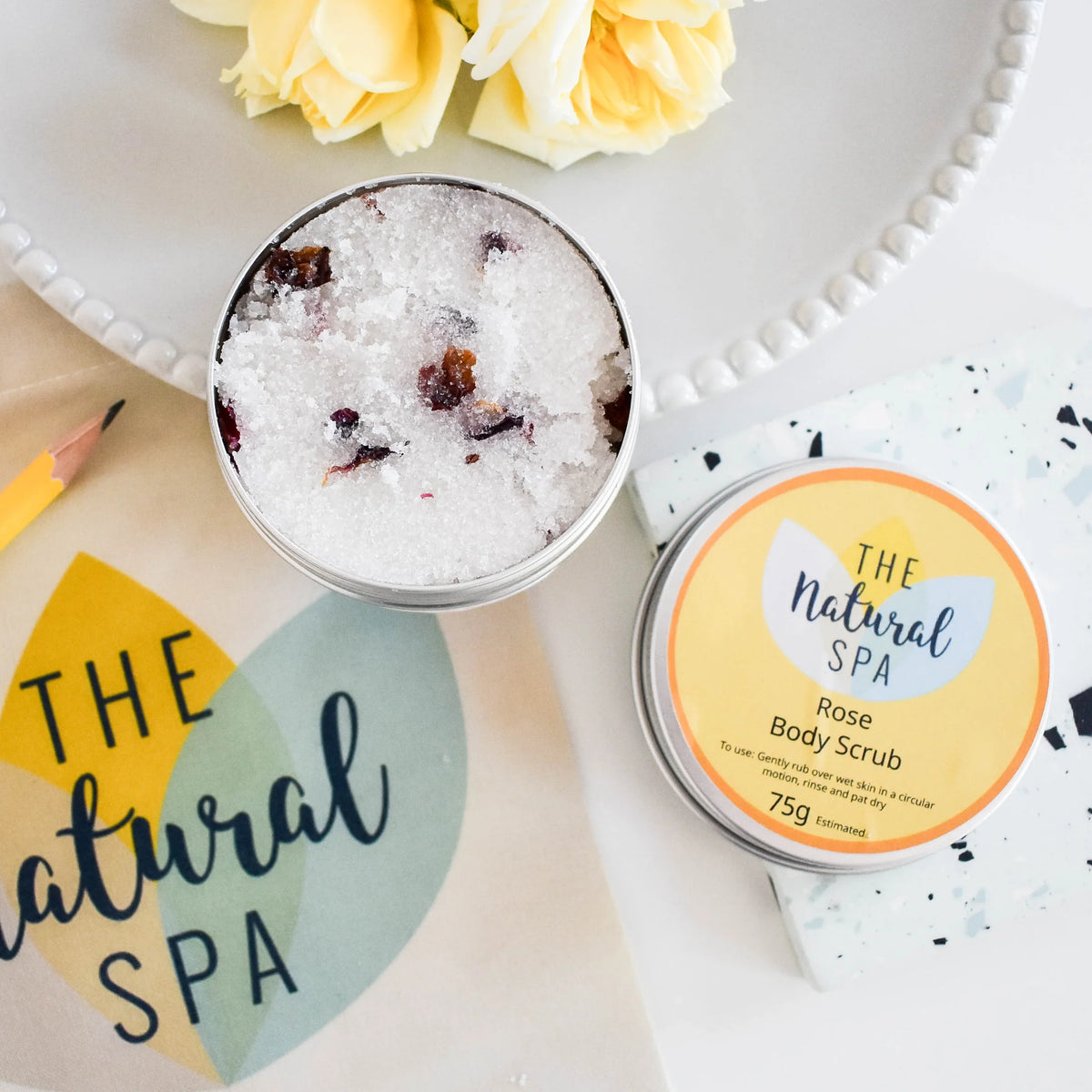 Rose body scrub in a tin with packaging labeled 'The Natural Spa' on a decorative tray.