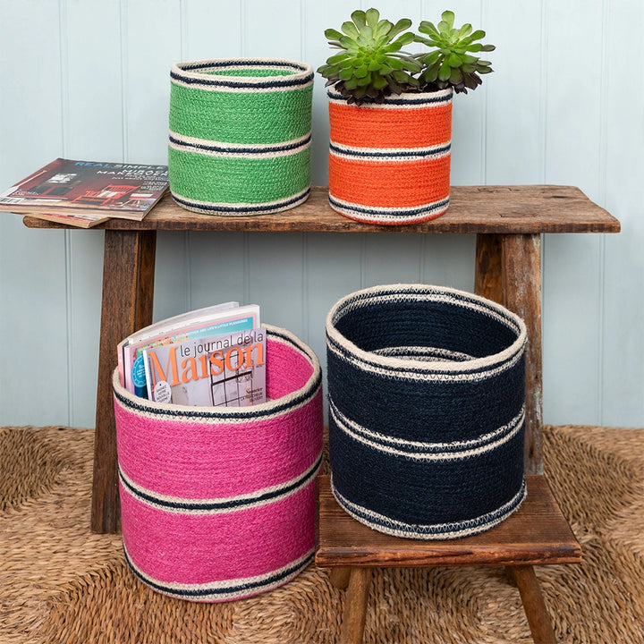 Colourful woven baskets with plants and a magazine on a wooden shelf.