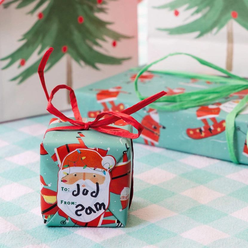 Christmas-themed gift box with Santa Christmas Gift tag Stickers on a checkered tablecloth.